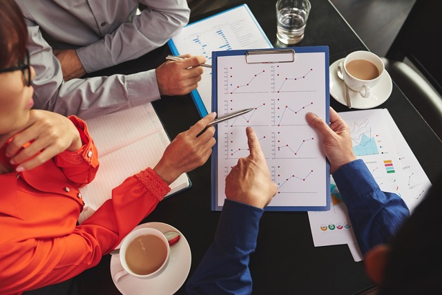 Business Professionals looking at a set of charts on a clipboard and pointing to data