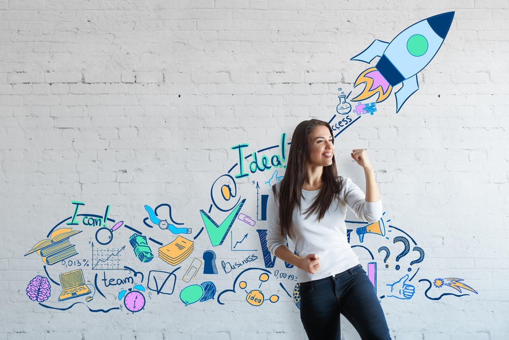 young woman cheering herself on standing in front of a white wall with inspirational art with a rocket ship taking off